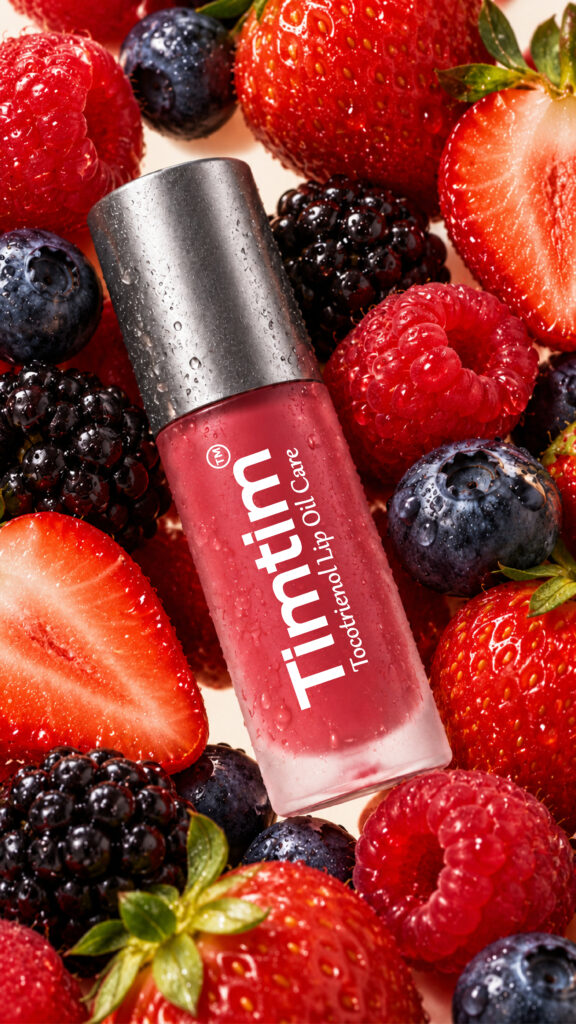 Timtim Mix Berries lip oil cream with a Titanium cap and water droplets among fresh mixed berries