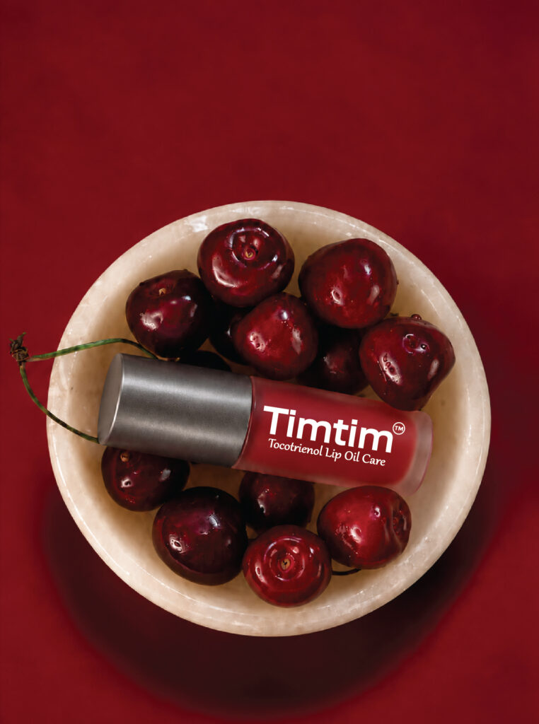 Timtim Cherry lip oil cream with a Titanium cap resting across a bowl of cherries