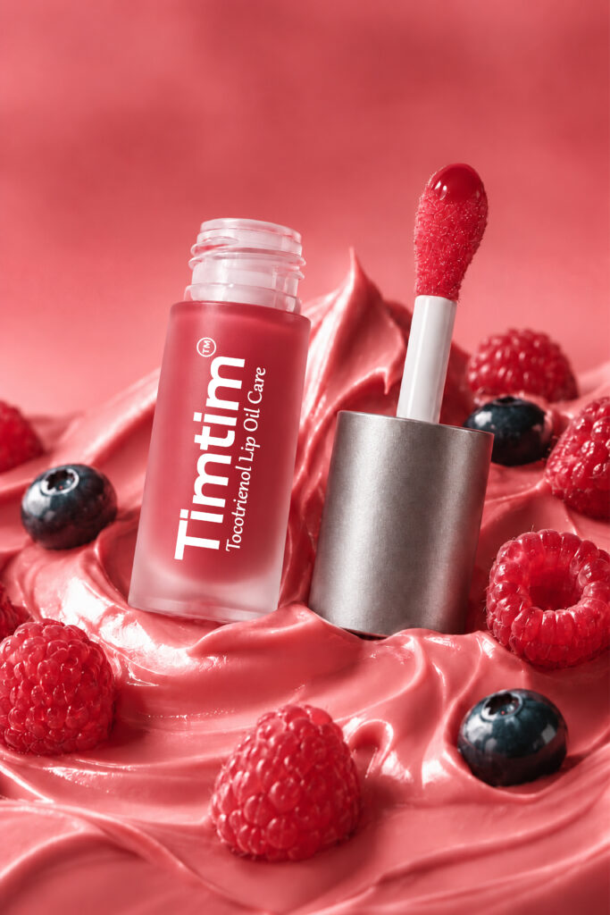 Open Timtim Mix Berries lip oil cream with a Titanium cap and applicator among raspberries and blueberries