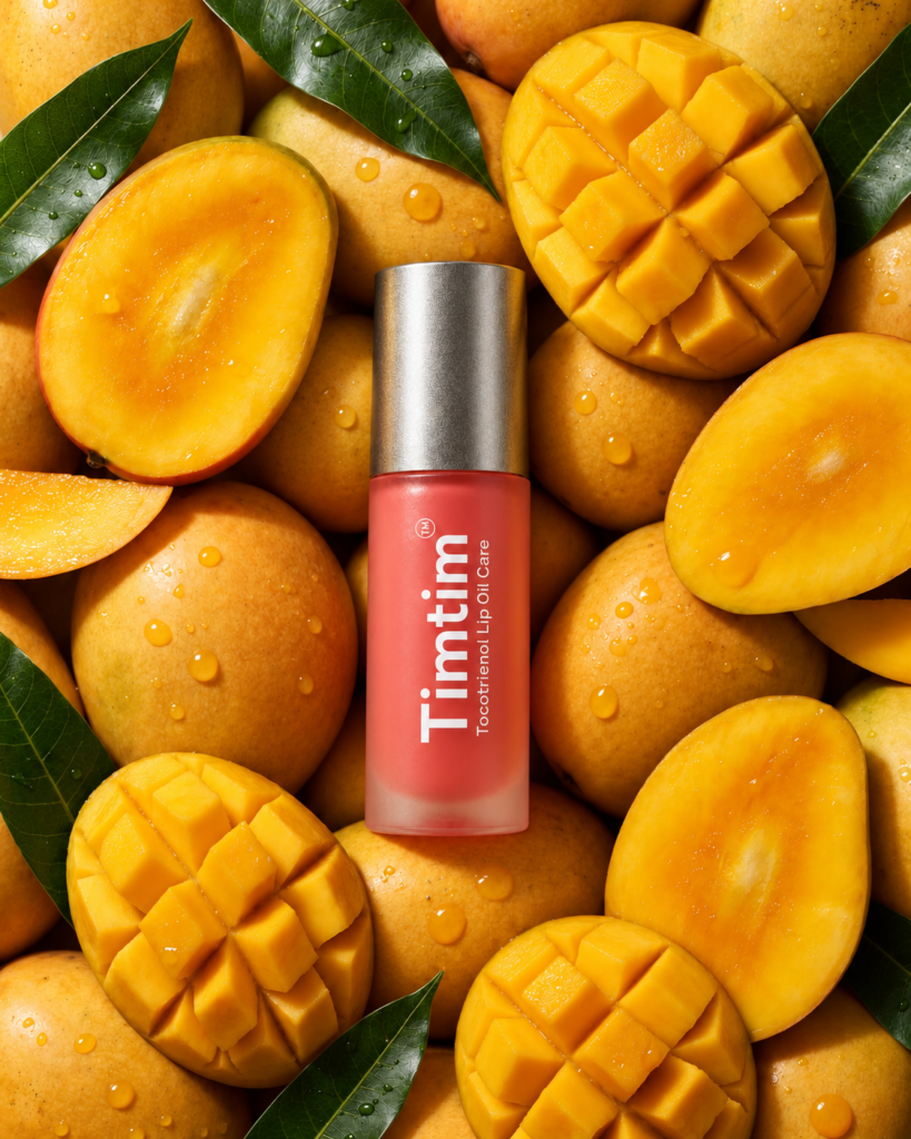 Timtim Mango lip oil cream with a Titanium cap surrounded by fresh mangoes and green leaves